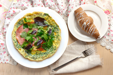 Breakfast with omelet, ham, basil and croissant.