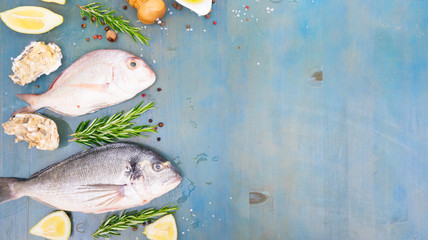 fresh sea fish set - dorada breams with lemon, herbs and spices on blue wooden background banner