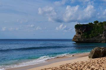 Beautiful beach ocean and blue sky. View on the rock and beach on tropical Island and landing airplane in the background.
