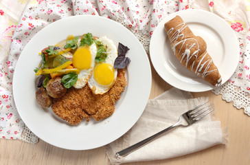 Breakfast with eggs, potatoes, schnitzel and croissant.