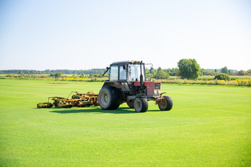 Tractor with a nozzle for care of a field lawn for a horse polo in work. The cut-off grass takes off from mechanical parts of a nozzle. Green flat field. lawn cultivation