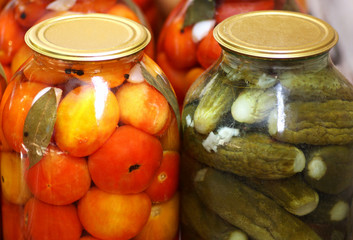 Glass jars with marinated red tomatoes and cucumbers.