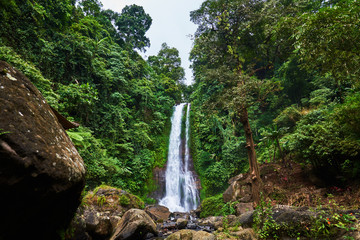 Fototapeta na wymiar Beautiful waterfall in green tropical forest. View of the falling water with splash of water makes. Nature landscape. Morning view on hidden majestic waterfall in the deep rain forest jungle. .