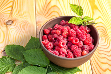 Fresh organic healthy raspberry with mint leaves in clay dish on wooden table background. Rustic style and natural light. food photo.