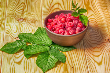 Fresh organic healthy raspberry with mint leaves in clay dish on wooden table background. Rustic style and natural light. food photo.