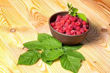 Fresh organic healthy raspberry with mint leaves in clay dish on wooden table background. Rustic style and natural light. food photo.