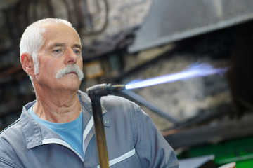 Senior man holding lit blow torch