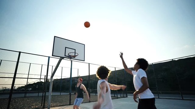 Smiling four multiethnic friends playing basketball together on playground
