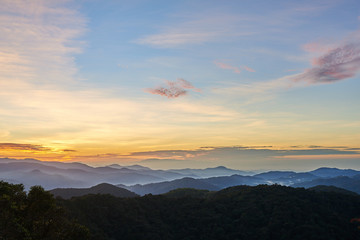 Mountain hill covered with forest on foreground and curly clouds on background with foggy valley with village in between. Mountains during sunrise. Beautiful natural landscape in the summer time..