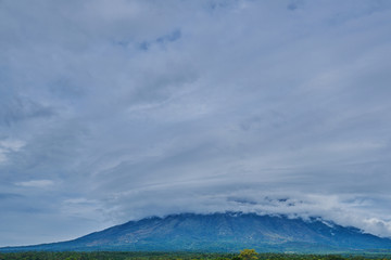 Picturesque view at the volcano peak covered in clouds. The green valley beneath the volcano.