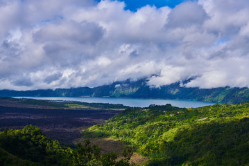 The Batur lake and volcano are in the central mountains in Bali, Indonesia. Beautiful natural landscape in the summer time. Mountains under clouds in the sun day. Natural background. Landscape.