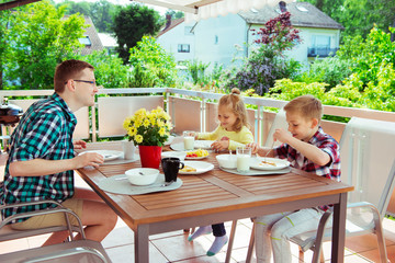 Happy young family having fun during breakfast on terrasse at home