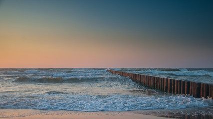 Sea waves at dusk with wooden breakwater and cloudless sky