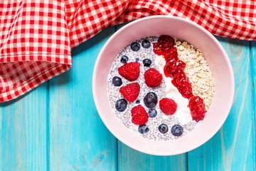 Smoothie bowl with chia seeds, muesli, jam and berries on blue wood background
