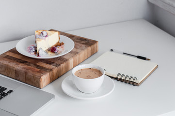 Сoffee cappuccino and dessert cheesecake at the work table with a notebook. concept of lunch in office at work. top view.