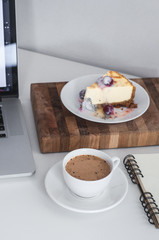 Сoffee cappuccino and dessert cheesecake at the work table with a notebook. concept of lunch in office at work top view