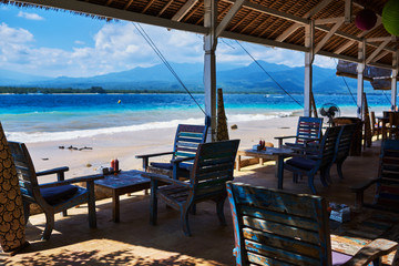 Leisure, travel and tourism concept - close up of table setting at empty open-air restaurant on the paradise beach. Wooden armchairs  on the background of a shining turquoise ocean. Tropical summer.