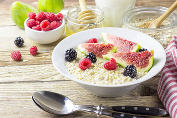 Bowl of oatmeal porridge with figs, raspberries and blackberries on teal rustic table, hot and healthy food for Breakfast, top view, flat lay