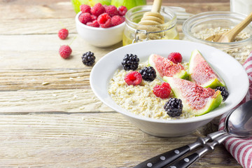 Bowl of oatmeal porridge with figs, raspberries and blackberries on teal rustic table, hot and healthy food for Breakfast, top view, flat lay