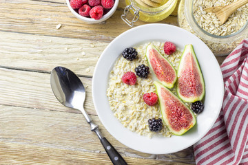 Bowl of oatmeal porridge with figs, raspberries and blackberries on teal rustic table, hot and healthy food for Breakfast, top view, flat lay