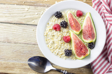 Bowl of oatmeal porridge with figs, raspberries and blackberries on teal rustic table, hot and healthy food for Breakfast, top view, flat lay
