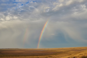 Rainbow in sky among  landscape over the boundless savannah, summer nature background, blue sky with clouds. The rainbow crosses the sky over desert. The concept of exotic tourism.