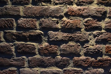 Closeup high-contrast photograph of a grungy brick wall, taken during the night. Light from an overhead lamp (lamp not shown) casts strong shadows and brings out the  rough features in the wall.