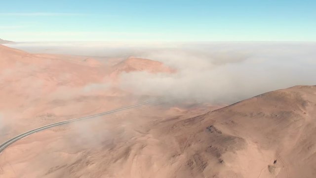 Aerial cinematic view of rocky sand dune, highway road with mist and fog. Atacama desert Iquique Chile. Drone flying forward and up tilting down at beautiful sunrise.