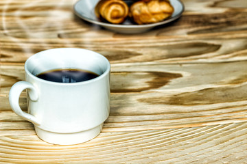 White cup with coffee and croissants on a wooden background, selective focus. The concept of breakfast.