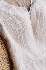 Close up white wedding dress with beautiful lace and beads lying on armchair. Bride's morning.top