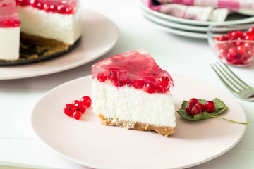 Slice of  cheesecake with red currant on top. Whole cake and serving plates in the background.