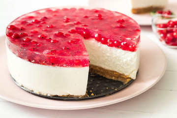 Round, white no bake cake with red currant on top, served on a plate.