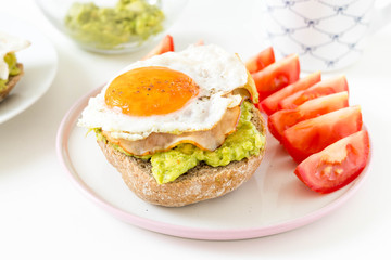 Breakfast sandwich with avocado, ham and eggs, served with fresh tomatoes and a cup of tea on white background.
