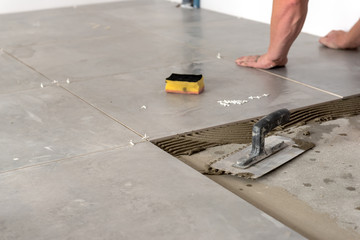 The hands of the tiler are laying the ceramic tile on the floor.