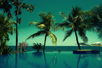 Obraz na płótnie Canvas Reflection of coconut trees in turquoise color swimming pool. Beautiful wiev at a beach resort in tropics. Palm tree and luxury hotel swimming pool at vacation times. Summer, vacation, travel concept