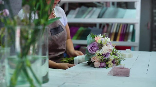 professional florist cutting flower stems with scissors in wedding bouquet in studio. Caucasian female master in apron creating floral composition. Floristry, handmade and small business concept