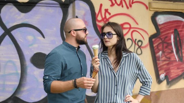 Playfully eating ice cream cones young people couple walk in a city having fun