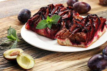 Rustic plum cake on wooden background with plums around.
