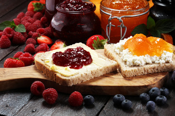 Toast bread with homemade strawberry jam and apricot marmalade on rustic table served with butter for breakfast or brunch
