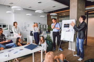 Corporate meeting of creative entrepreneurs in the office, a man standing behind a magnetic Board with funding schedules