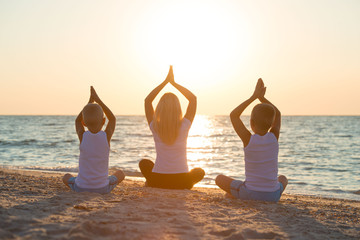Mother and children do exercises on the beach, they meet the sunrise.Fitness, sport, yoga and healthy lifestyle concept.
