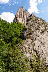 High mountain peak and forest against blue sky with clouds in Turda gorge, Romania
