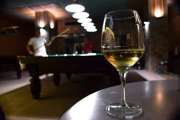 A glass of white wine on a table with billard table on a background