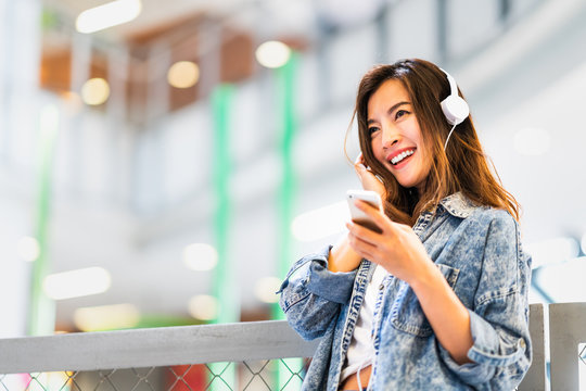 Beautiful young Asian girl listen to music using smartphone and headphone smile at copy space. Modern teenager lifestyle, college student hobby, youth culture or mobile phone gadget technology concept
