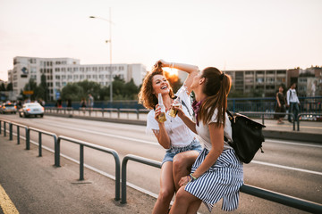 Two girls laughing and drinking on the bridge.