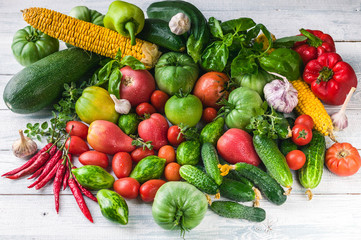 Red and green tomatoes, corn, red pepper, cucumbers, garlic, basil and marjoram on a light wooden background. Autumn Harvest Concept