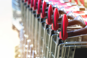 View of row of stacked shopping carts with red handles at exit of supermarket at day mall on parking lot in Europe. Buy food supplies with transport