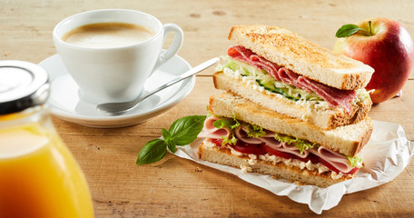 Cup of coffee and sandwich with ham on table