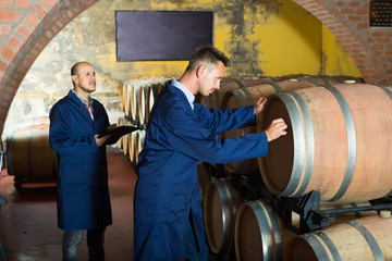 Obraz na płótnie Canvas two men in uniforms taking notes in cellar with wine woods