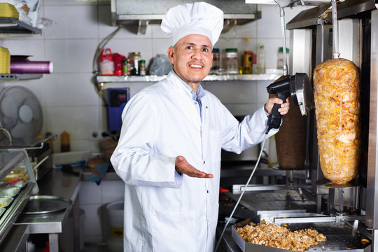 Cheerful mature man cook cutting kebab meat on kitchen